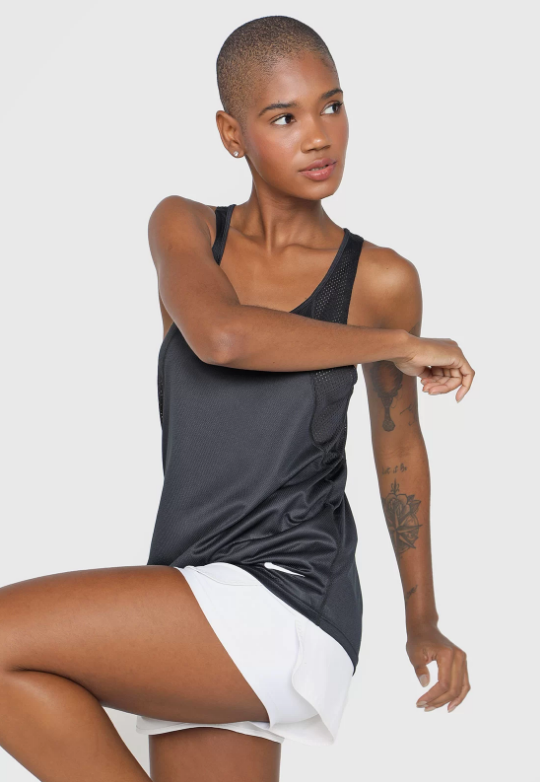 Uma mulher negra se alonga utilizando uma regata cinza e shorts branco