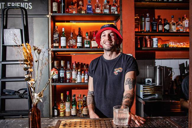 Rapaz de gorro em balcão de bar com drinque na mão