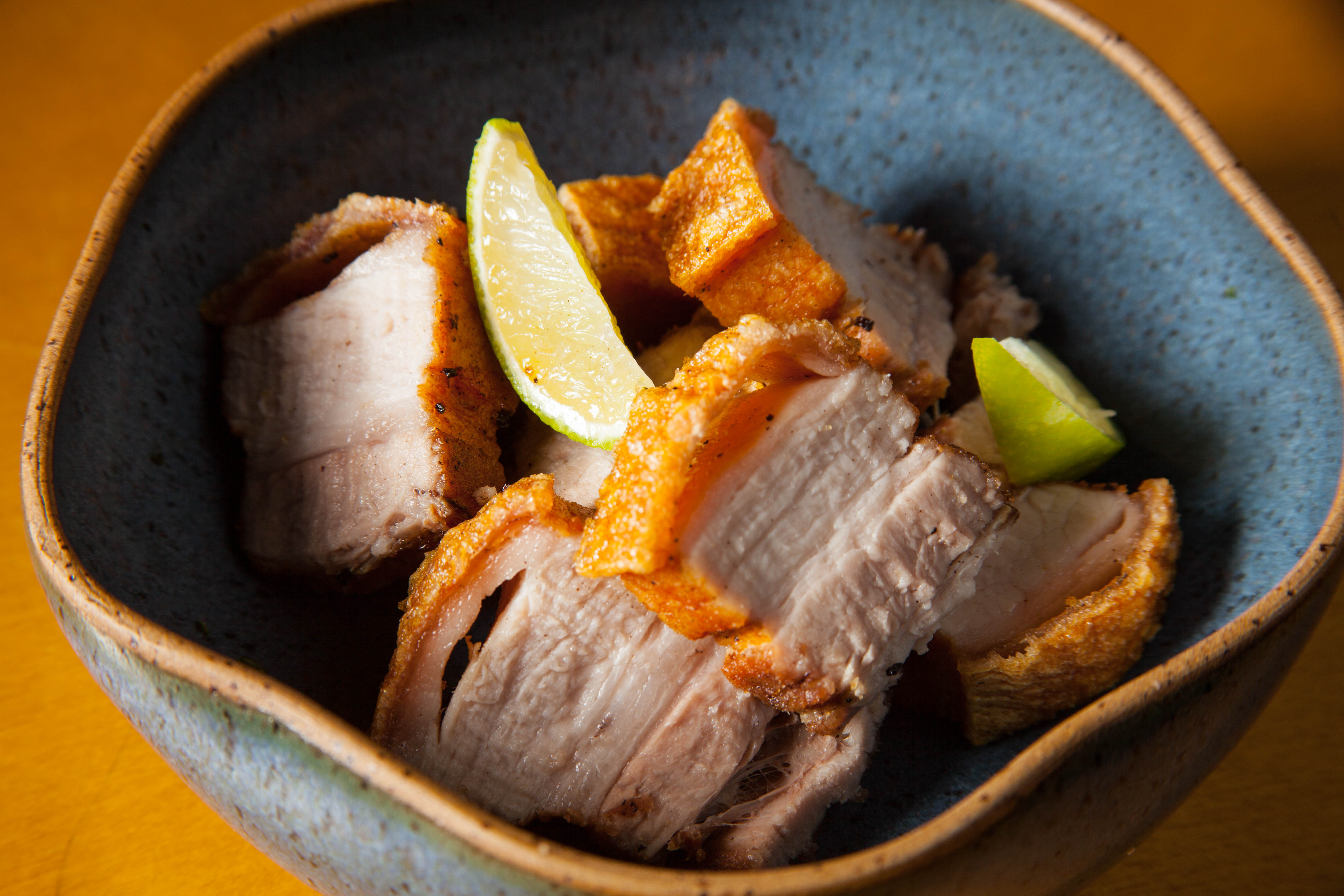 Pote de cer&acirc;mica azul com quadradinhos de torresmo dentro e fatias de lim&atilde;o.