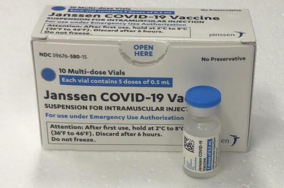Imagem mostra uma embalagem branca e azul próxima a um frasco transparente. É possível ler "Janssen COVID-19 Vaccine" na lateral da embalagem.
