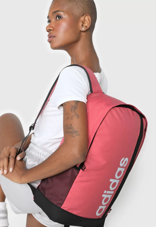 mochila Uma mulher negra está meio de costas segurando uma mochila rosa nas costas