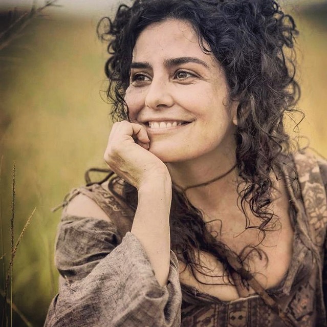 Retrato da atriz Letícia Sabatella, ela tem os cabelos longos e uma das mãos, apoiando o rosto
