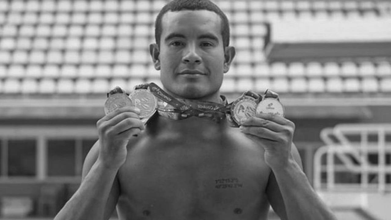 Ian aparece sem camisa, diante de piscina, segurando medalhas de competições