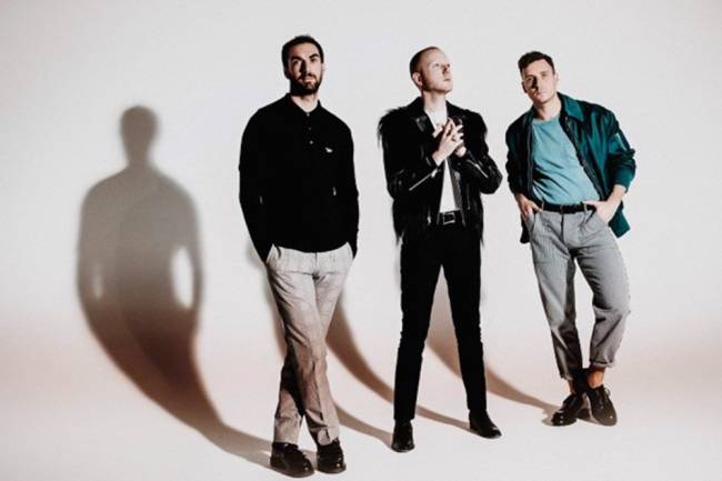 Two Door Cinema Club.jpg Imagem mostra três homens em frente a parede branca.