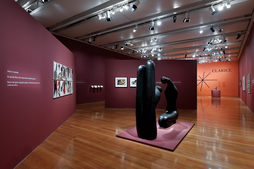 notaabre_crédito_julia_thompson_1.jpg Foto de uma sala de galeria. A parede é vermelha, uma luz fraca ilumina uma escultura.