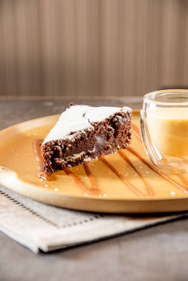 Torta de chocolate servida junta de um pequeno recipiente de vidro com creme