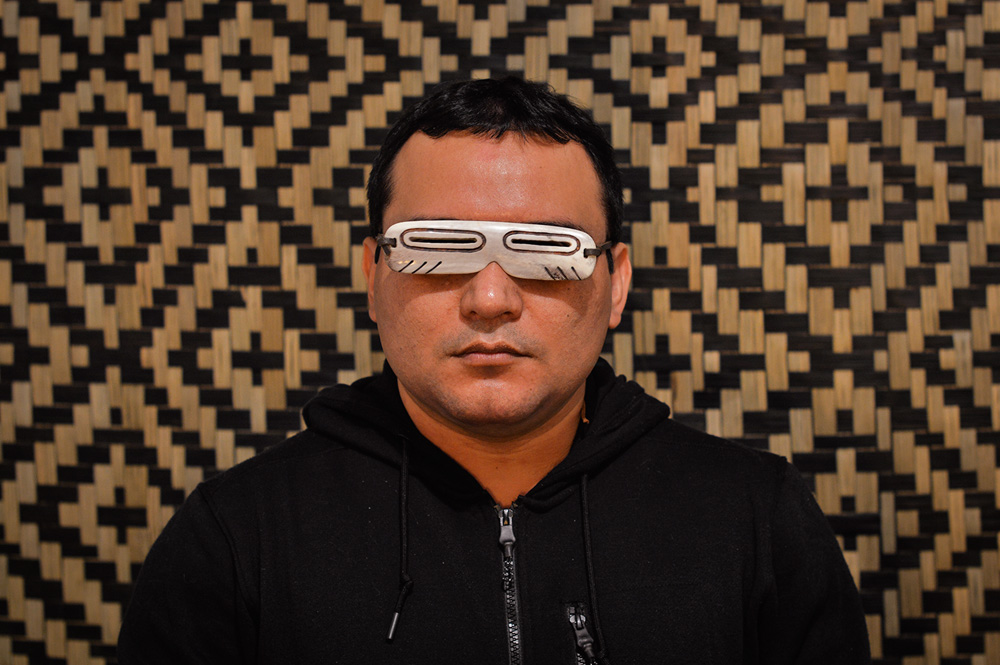Créditos_DenilsonBaniwá.jpeg Imagem mostra homem de casaco preto com uma espécie de óculos metálico sobre os olhos.