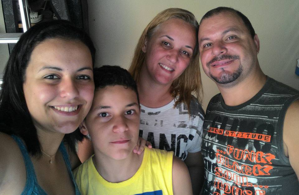 Imagem mostra família abraçada e sorrindo. À esquerda, uma mulher sorrindo, à direita, um casal mais velho e no centro um menino.