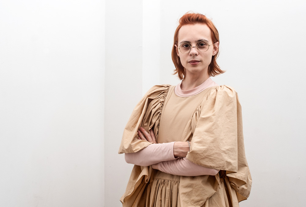 ph renato custodio.jpg Pessoa de cabelo ruivo vestindo roupa bege, com uma parede branca de fundo.