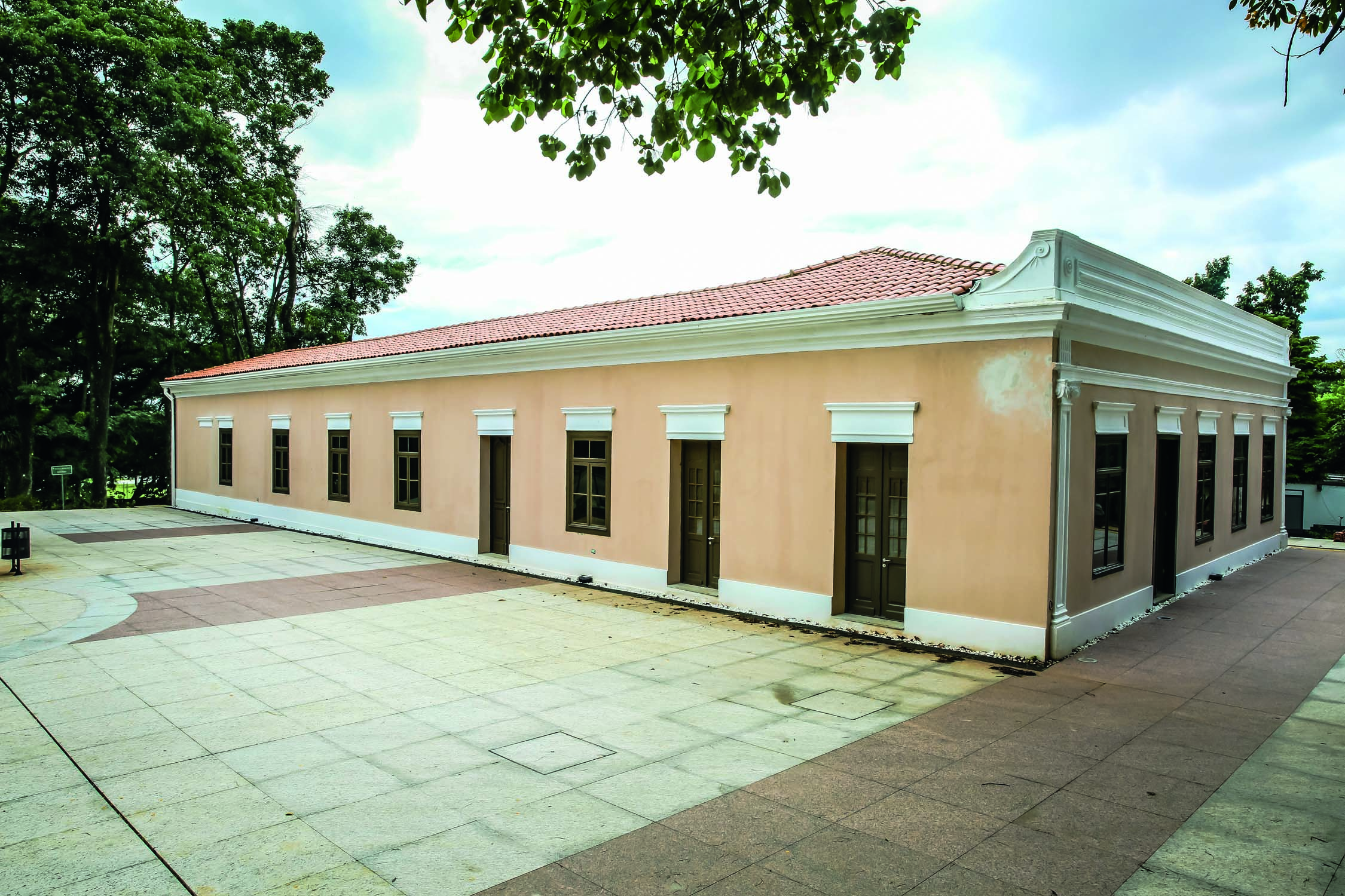 Imagem mostra constru&ccedil;&atilde;o de paredes amareladas, telhado de tijolos e diversas janelas e portas marrons.