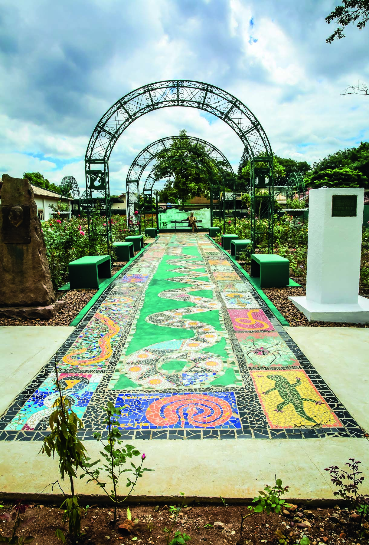 Imagem mostra ch&atilde;o de azulejos com desenhos de cobras. Ao fundo, um banco com uma est&aacute;tua de bronze.