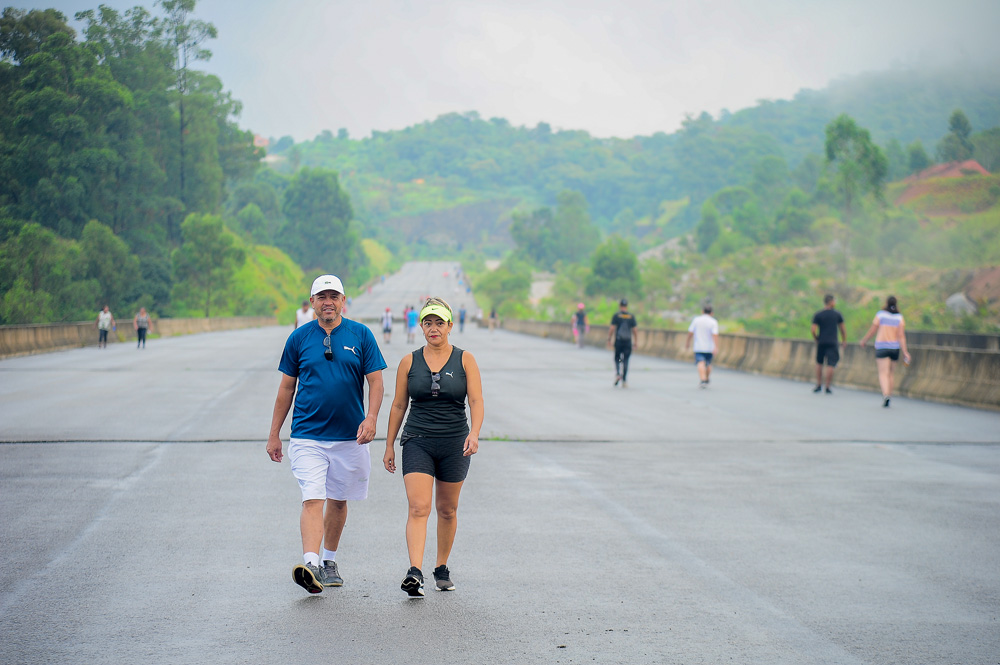 Um homem e uma mulher usam roupa de ginástica e caminham pelo rodoanel inacabado