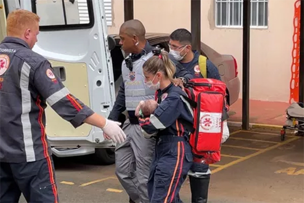 Imagem mostra bombeira carregando bebê até ambulância, na área de estacionamento de condomínio residencial