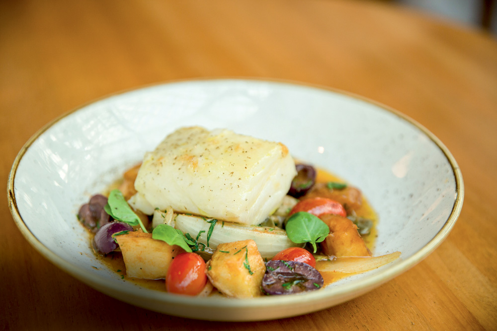 Bacalhau servido em cerâmica junto de azeitona preta, batata e tomate