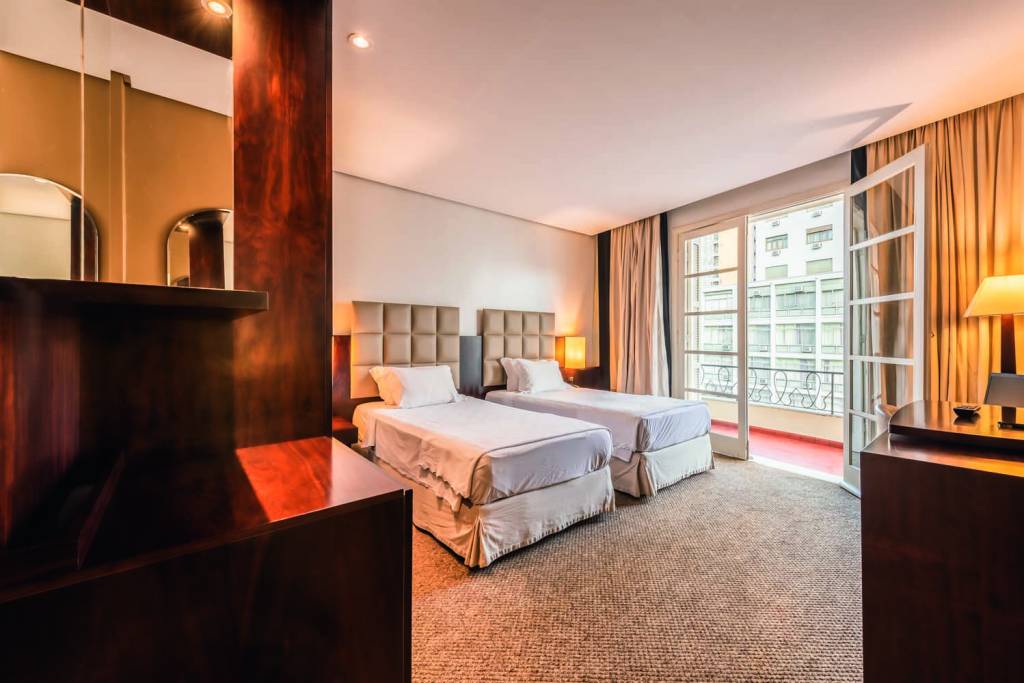 Quarto solteiro no prédio antigo.jpg Imagem mostra quarto de hotel com duas camas e varanda