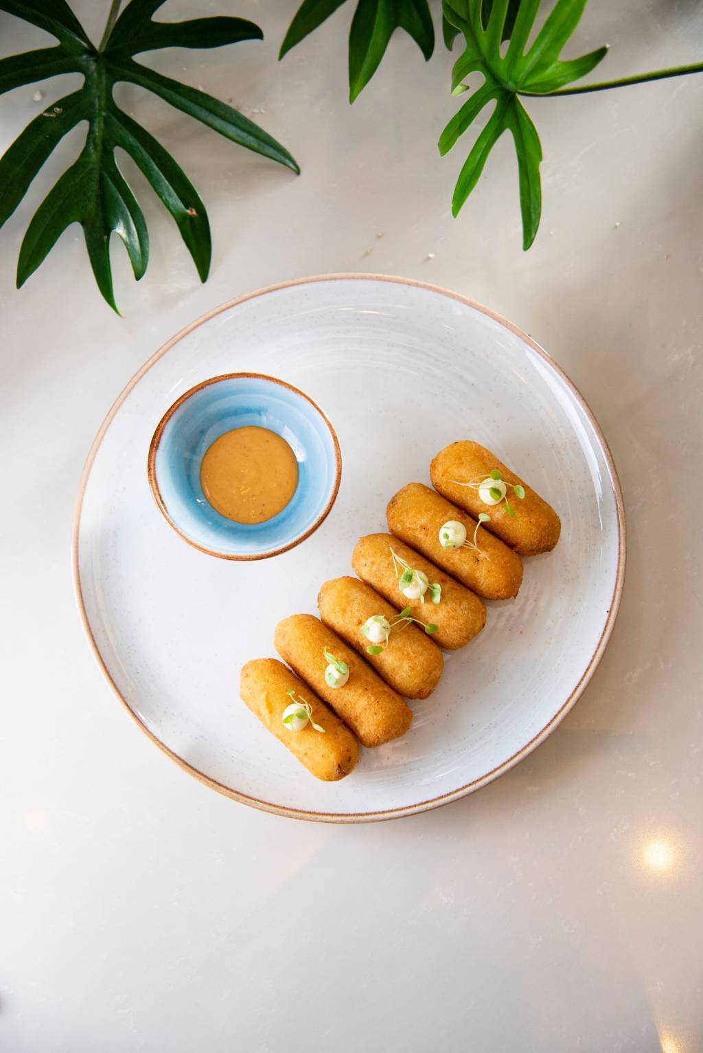 Bolinho caipira (carne, milho e molho de pimenta da casa) – Terraço Jardins Imagem de vários bolinhos enfileirados no prato e um potinho azul com o molho