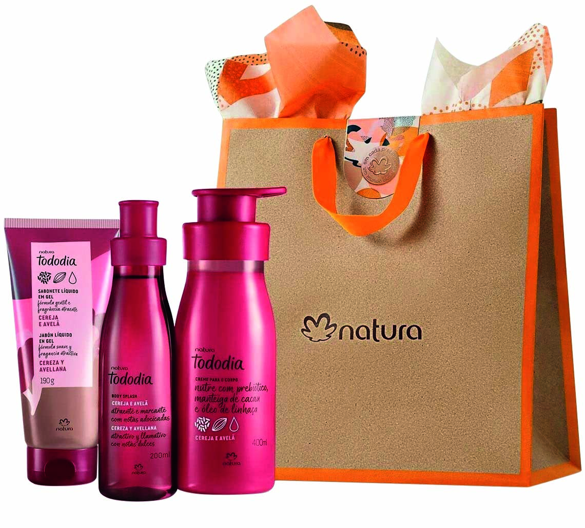 Kit de cremes da Natura. Tr&ecirc;s frascos de formatos diferentes, todos na cor rosa pink, ao lado de uma sacola de papel&atilde;o com detalhes em laranja e o nome da marca no centro