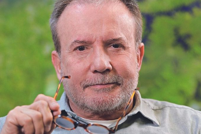 Luiz Carlos é um homem de meia-idade, calvo, de cabelos e barba grisalhos. Ele é um homem branco de olhos castanhos. Olha para a câmera com um óculos de armação tartaruga em uma das mãos