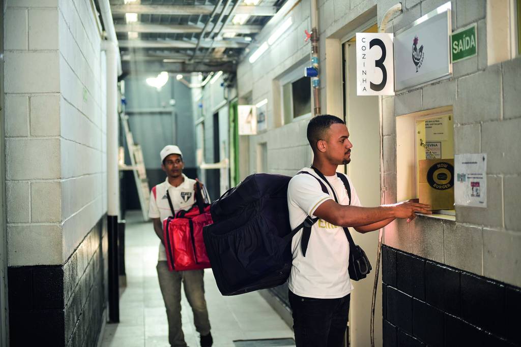 EDITADAS VEJA SP28.jpg Imagem mostra dois homens em corredor, com bolsas de aplicativos de delivery