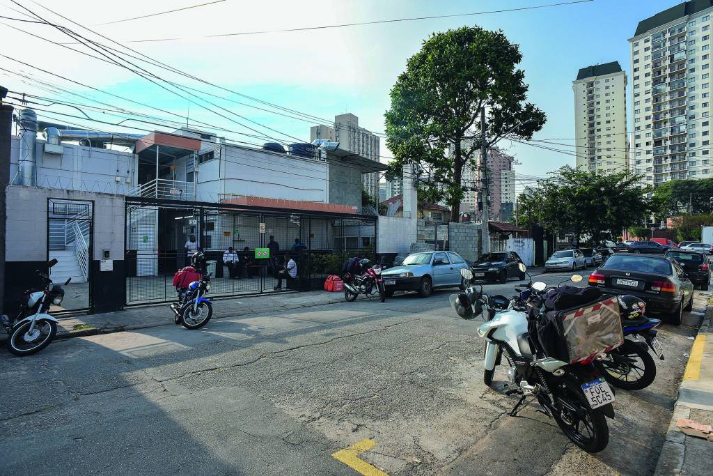 EDITADAS VEJA SP37.jpg Imagem mostra rua com carros e motos estacionados. Ao fundo, um portão.