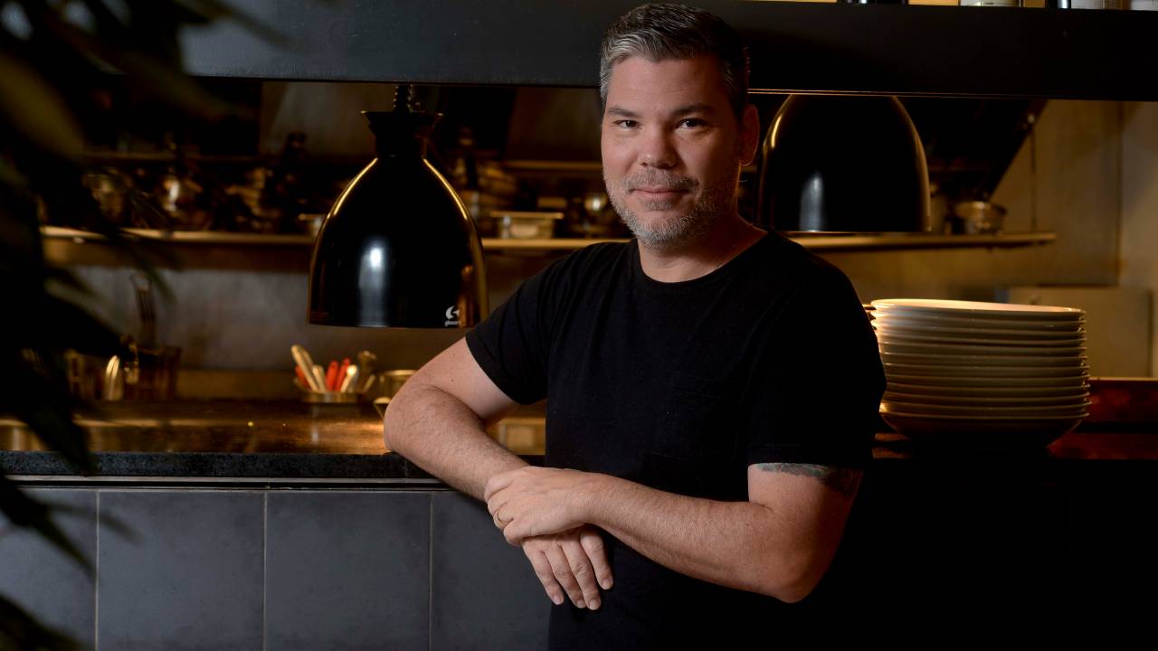 Pedro Artagão posa diante da cozinha com os as mãos cruzadas à frente do corpo