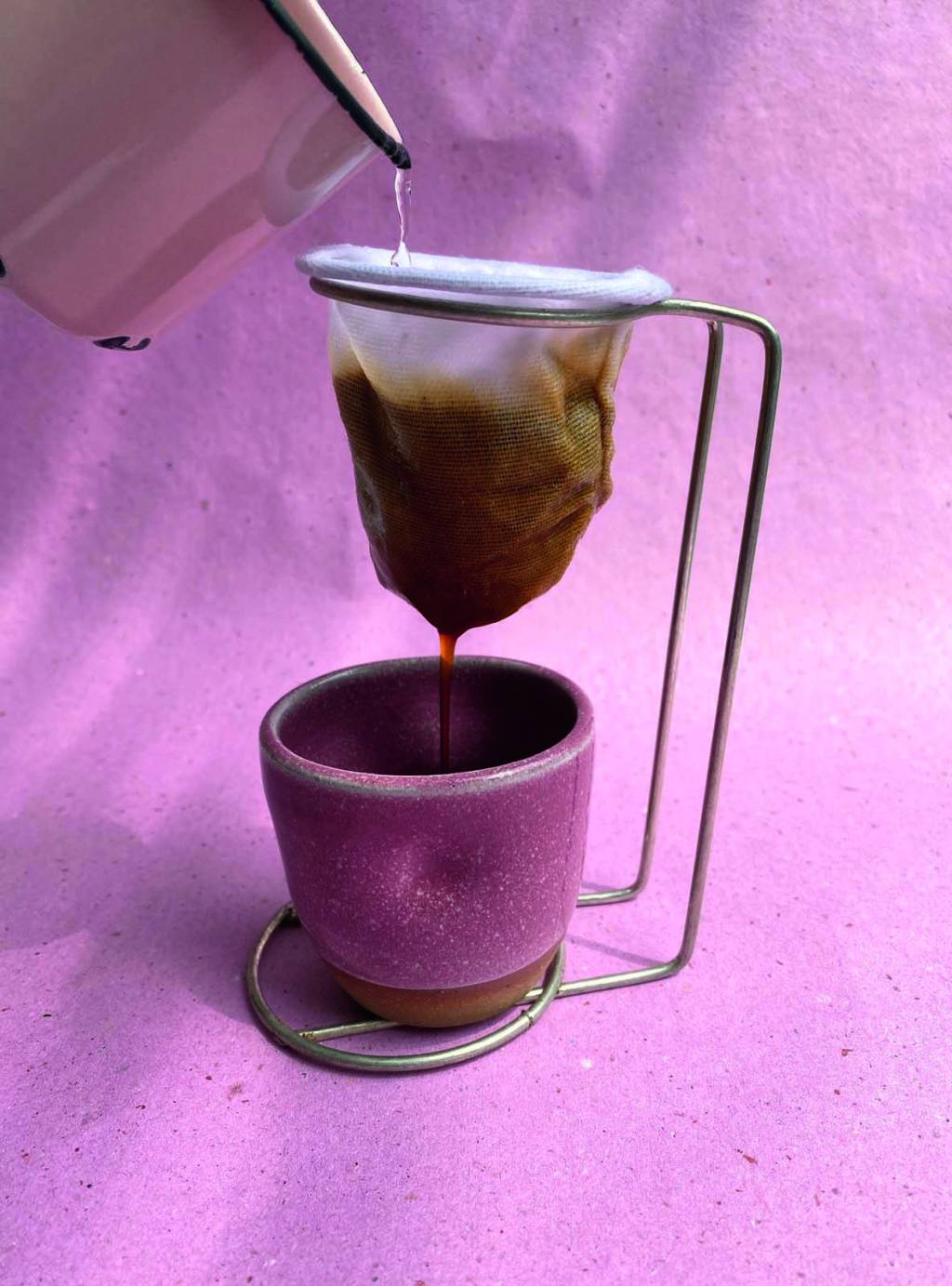 A Baianeira Masp Foto de uma xícara de café de cerâmica rosa embaixo de um coador na frente de uma parede de cor rosa