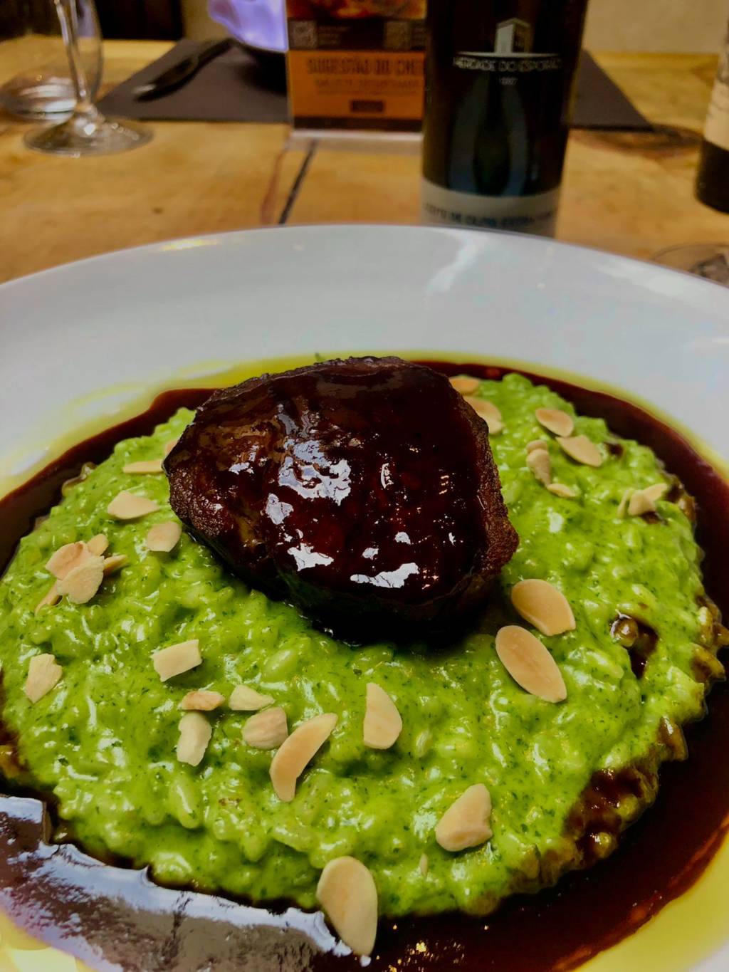 Altruísta Osteria & Enoteca Risoto de cor esverdeada salpicado com lascas de amêndoas e., sobre ele, um medalhão de fié-mignon