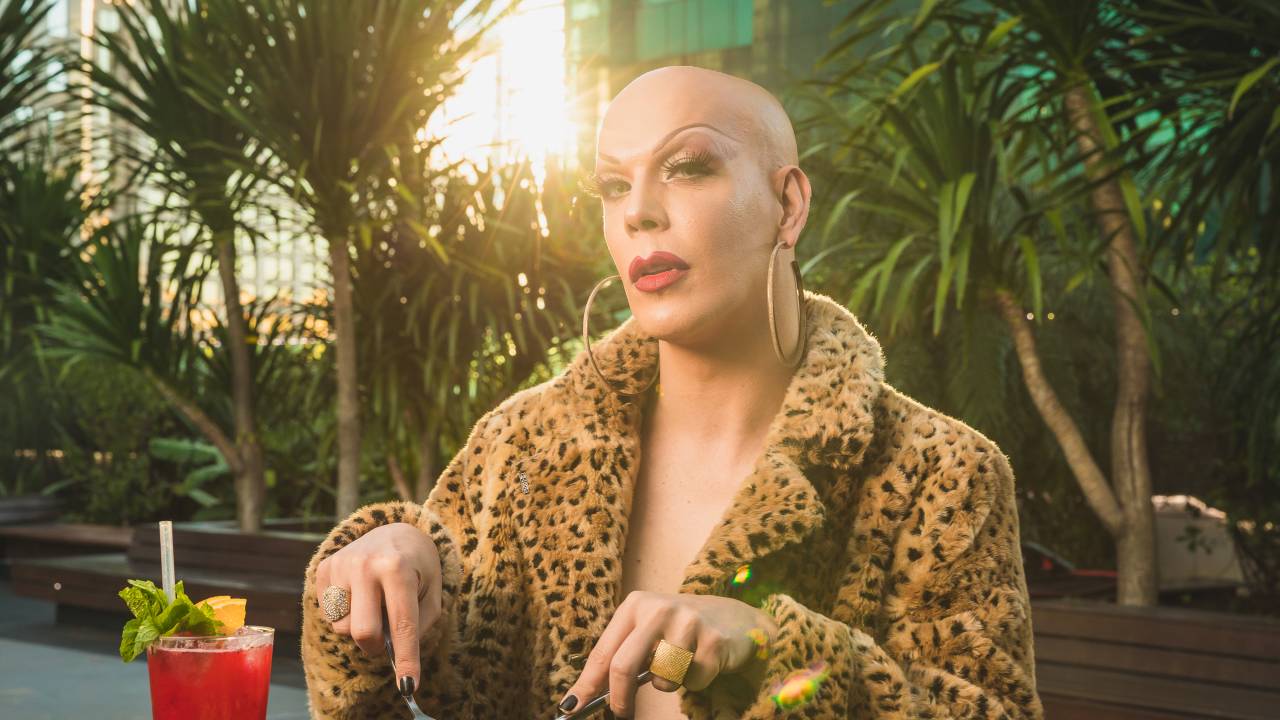Drag queen com mãos em talheres, como se estivesse comendo