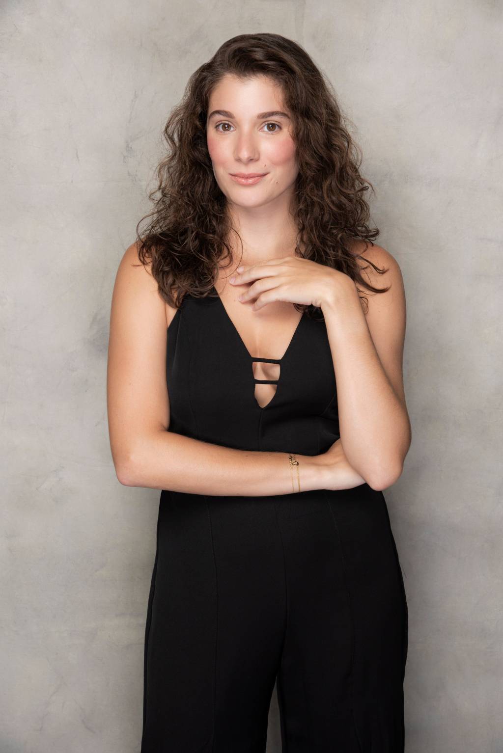 Giulia Bertolli (Pino Gomes) Giulia Bertolli posa com uma das mãos gentilmente pousada no colo e a outra na cintura. Ela encara a câmera, tem cabelos castanhos encaracolados e veste um vestido preto.