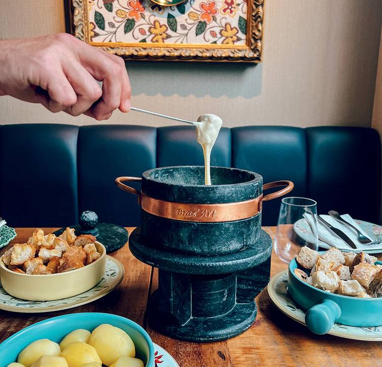 uma mão mergulha um pedaço de pão no fondue de queijo