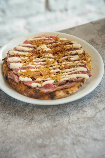 Ribeye tonatto: lâminas do corte, maionese de leite, molho de atum, aliche, alcaparras e crisps de cebola sobre disco de massa de pizza