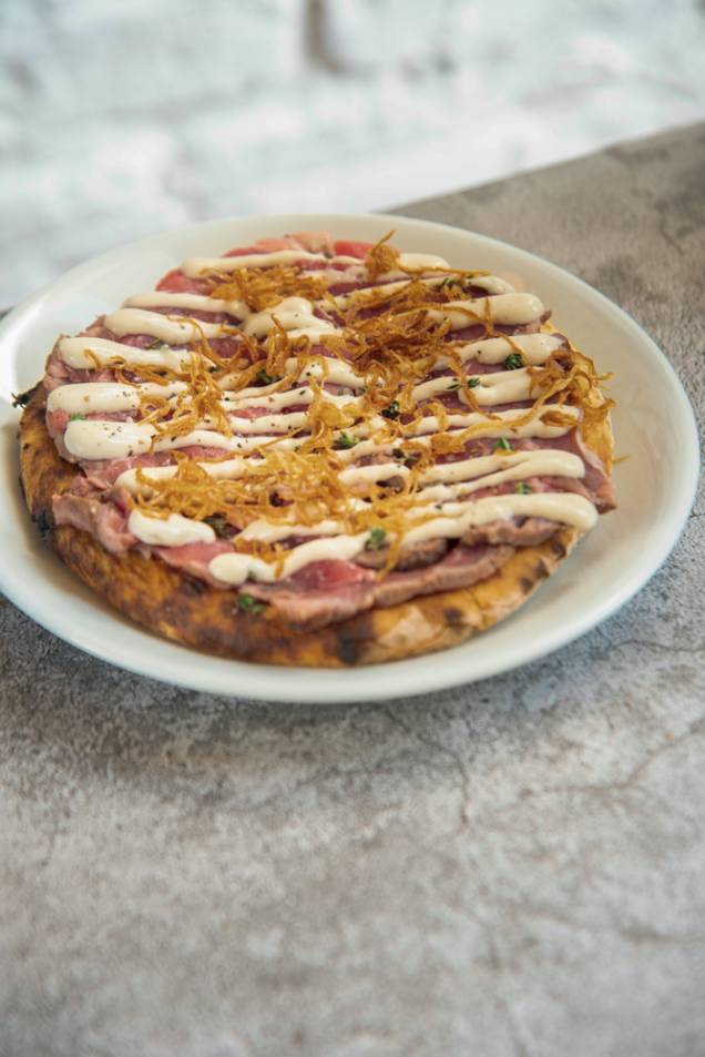 Ribeye tonatto: lâminas do corte, maionese de leite, molho de atum, aliche, alcaparras e crisps de cebola sobre disco de massa de pizza Ribeye tonatto: lâminas do corte, maionese de leite, molho de atum, aliche, alcaparras e crisps de cebola sobre disco de massa de pizza