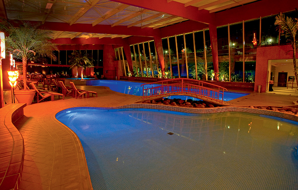 Villa Rossa (Eduardo Santana).jpg Foto exibe piscina interna iluminada e pequena ponte que a divide em duas áreas.