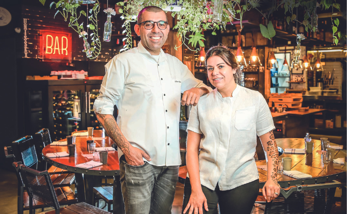 Imagem mostra casal de chefs de roupas brancas, sorrindo.