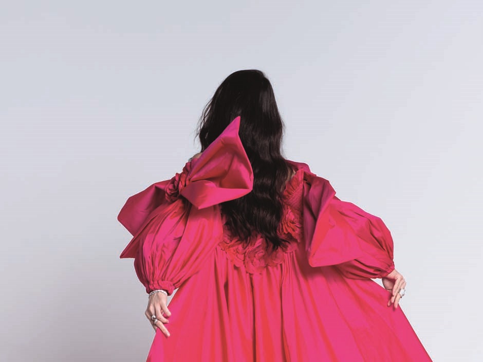 Mulher de cabelos pretos posa de costas em longo vestido rosa choque.