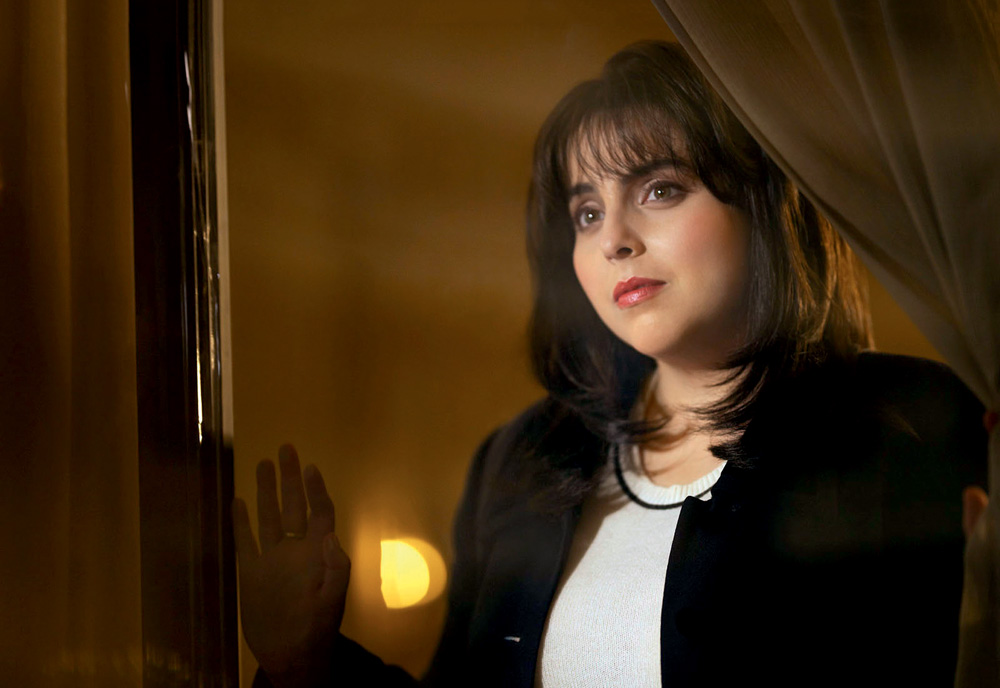 Imagem mostra mulher de blazer preto olhando pela janela