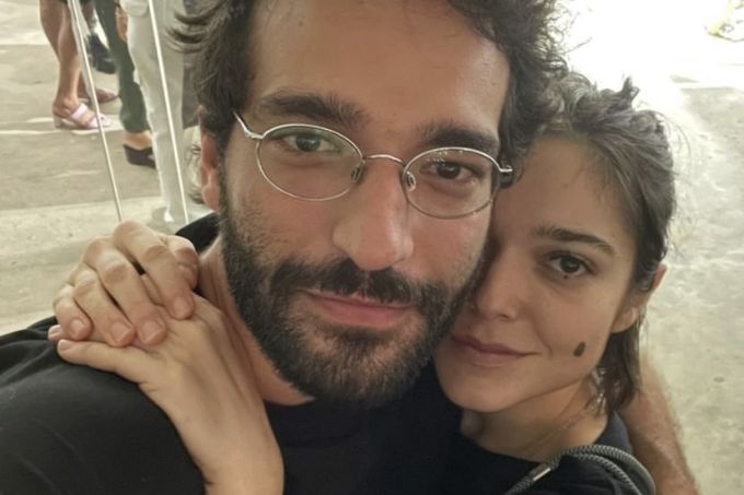 Foto de Humberto Carrão usando óculos e Bella Camero abraçada, com mão em seu ombro e rosto colado
