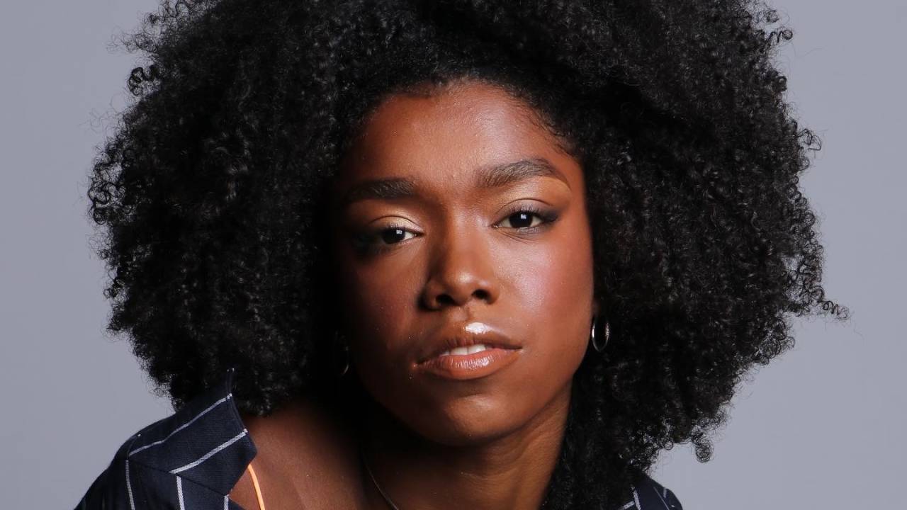 Dançarina Trislane Martins, mulher negra com black power vestindo blusa escura com listras brancas.