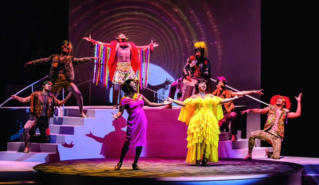 Crédito_ Caio Gallucci_Divulgação .jpg No palco, duas cantoras negras interpretam Alcione enquanto cantam. Uma usa um vestido amarelo bufante e a outra, um vestido midi rosa. Outros atores estão atrás, com figurinos coloridos