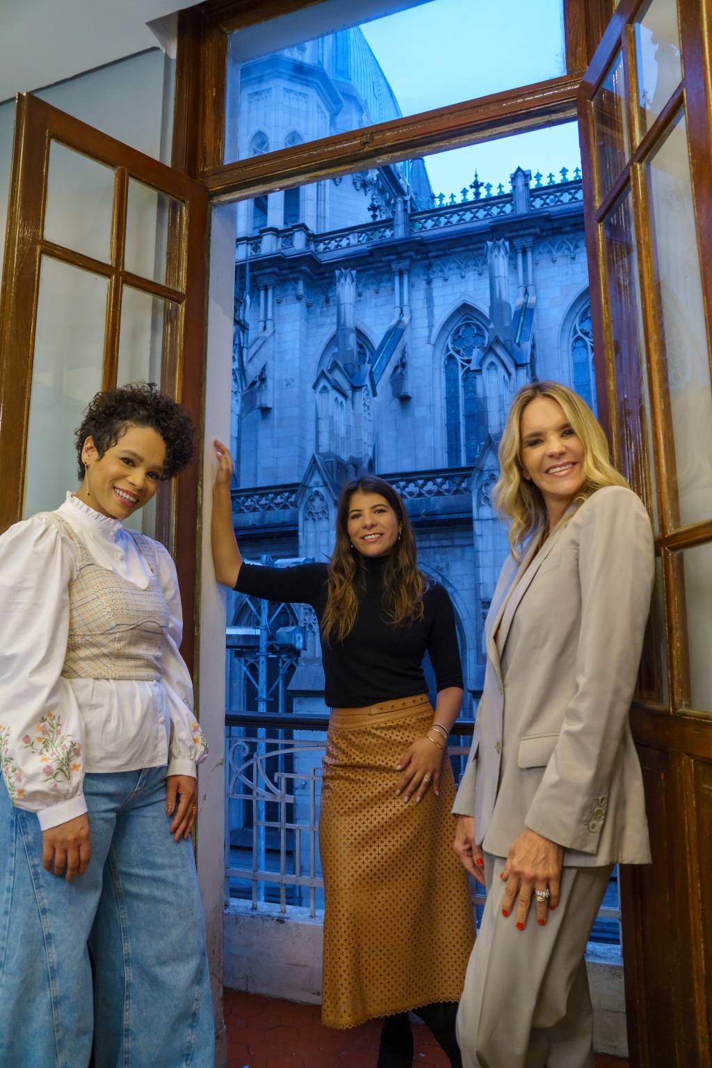 StyleBar (Renato Borges-Divulgação) (1) Tatiane, Bianca e Deborah (a partir da esquerda) posam de pé olhando para baixo na câmera. As três estão de pé perto de uma janela com vista para a Catedral da Sé.