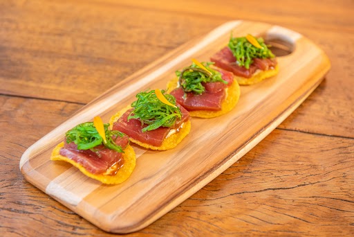 tostada de atum miya Quatro tostadas de milho com atum marinado sobre elas, dispostas sobre uma tábua de madeira para servir
