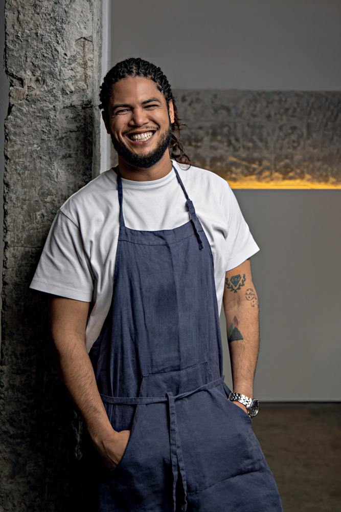 2022_08_28_Comer_e_Beber_Rodrigo_Wanezza_Soares-6637-Edit.psd Imagem mostra homem de avental cinza sobre camisa branca sorrindo
