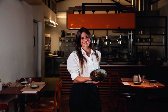 Chef Elisa Fernandes mostra conteudo de cumbuca de cerâmica em ambiente da cozinha