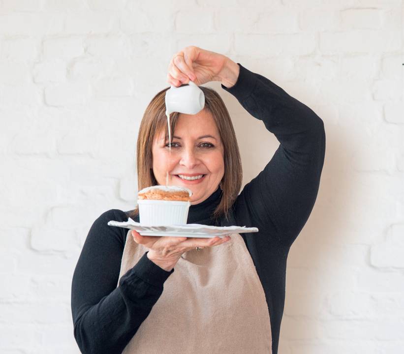 Chef Carla com um prato na mão contendo um suflê sobre o qual despeja o conteudo de um minibule de porcelana, creme de catupiry