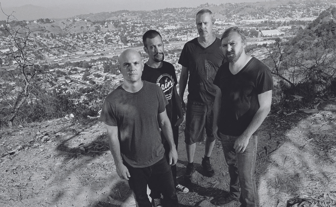 Imagem em preto e branco mostra quatro homens com uma cidade ao fundo
