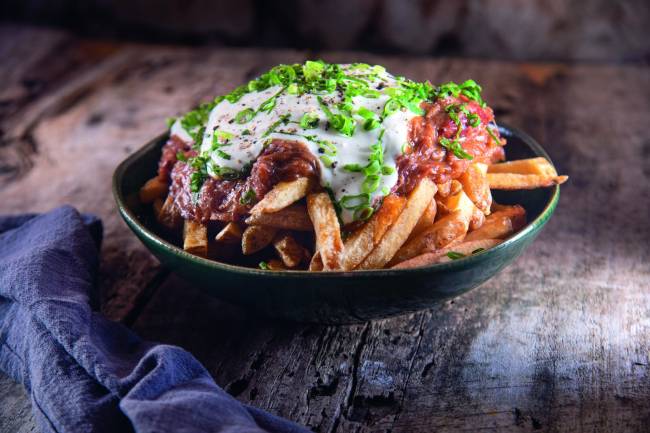 Recipiente preto contendo batatas fritas cobertas por carne desfiada, creme azedo e cebolinha