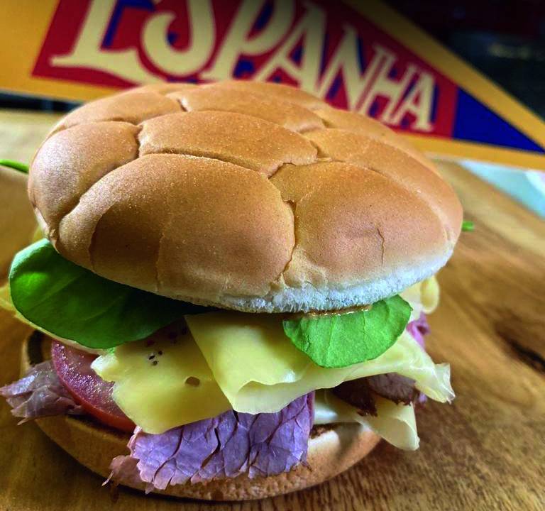 Lanche em pão com desenho de bola de futebol sobre tábua de madeira com uma flâmula ao fundo onde se lê Espanha