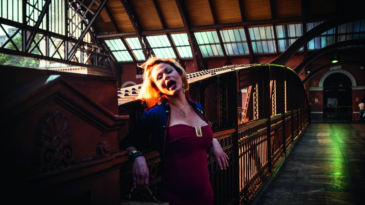 Imagem mostra mulher de vestido vermelho brindo a boca em estação de metrô