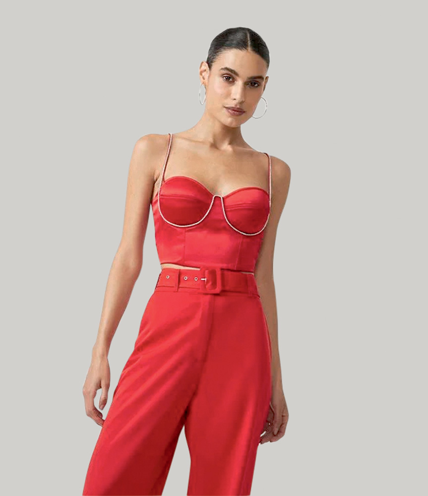 Modelo branca, magra, de cabelos escuros em um coque usa cropped de cetim vermelho com aplica&ccedil;&atilde;o de strass no busto