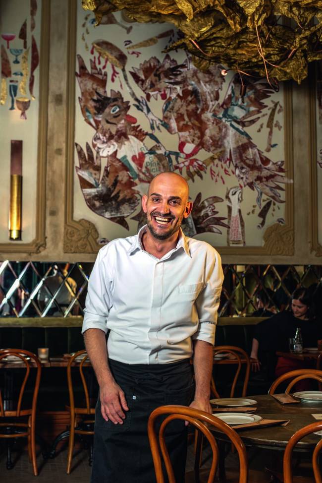 Gerard Barberan Il Capitale Homem de camisa branca e calças escuras à frente de tapeçaria em ambiente interno